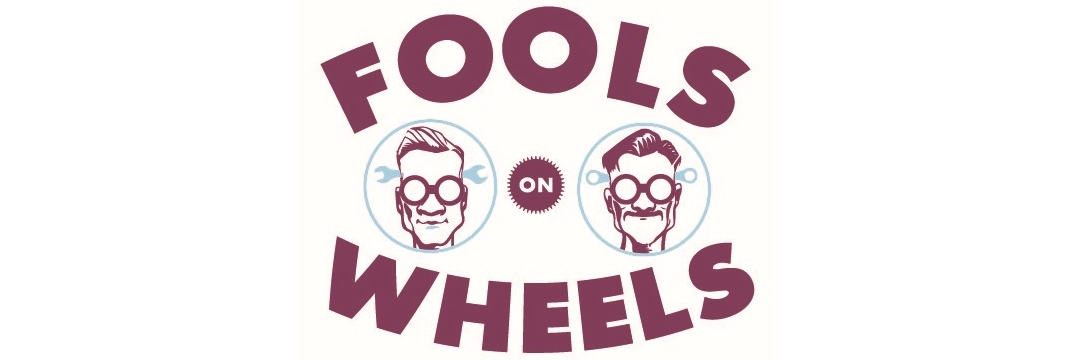 Logossa lukee "Fools on Wheels" violetilla tekstillä, ja siinä on kaksi sarjakuvahahmoa silmälaseissa, joilla on työkalut ympärillään.