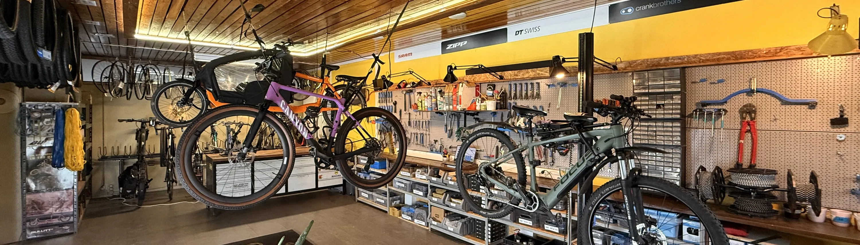 Polkupyöräliike, jossa on esillä polkupyöriä, työkaluja ja tarvikkeita, valaistus on kirkas ja värit ovat monipuoliset.